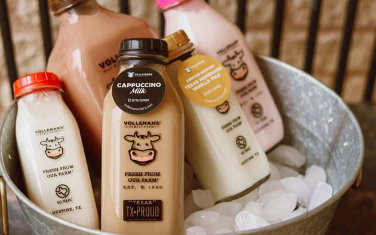 5 botellas de vidrio que muestran diferentes sabores de leche en un balde que se enfría en hielo.